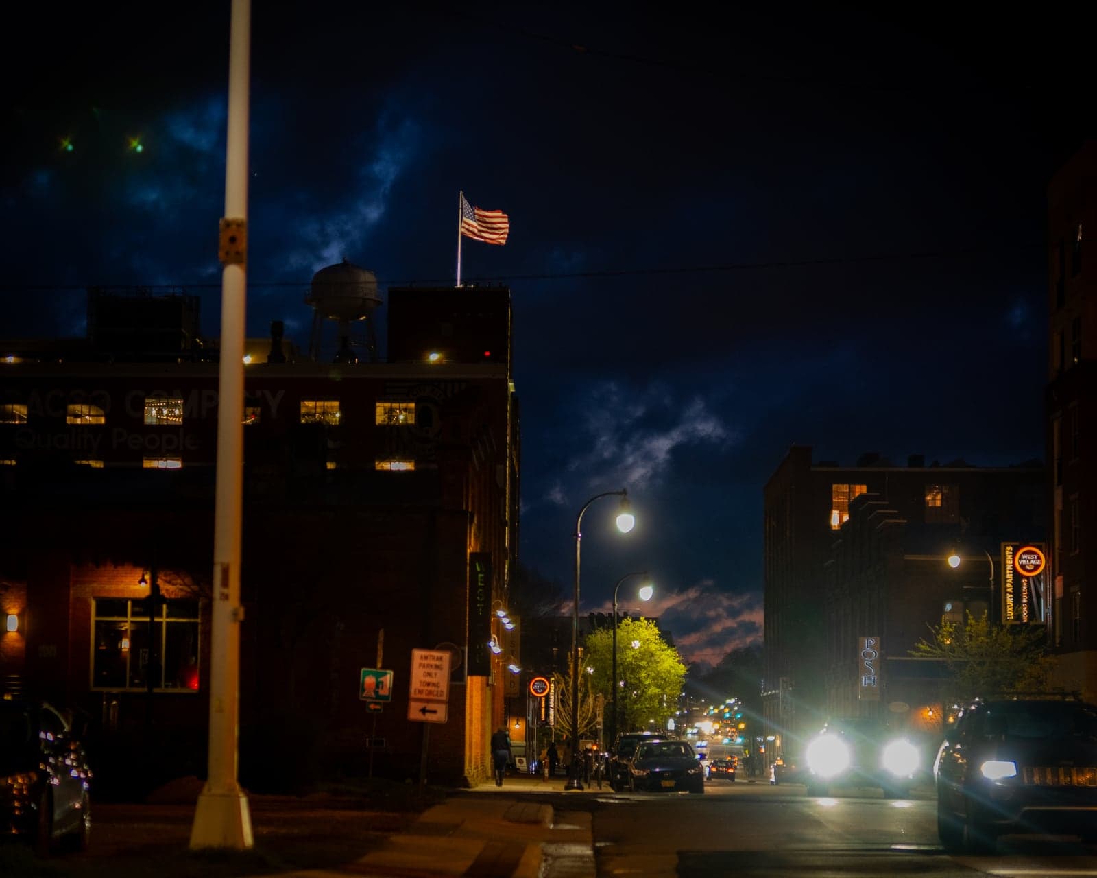 Durham's West Village lit up at dusk, water tower and flag overhead