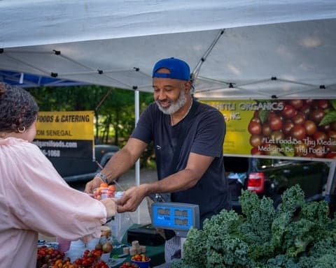 Farmers market vendor handing a customer fresh kale