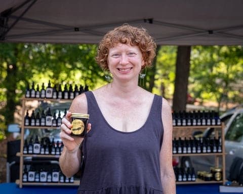 Vendor holding a jar of preserves at her market stand